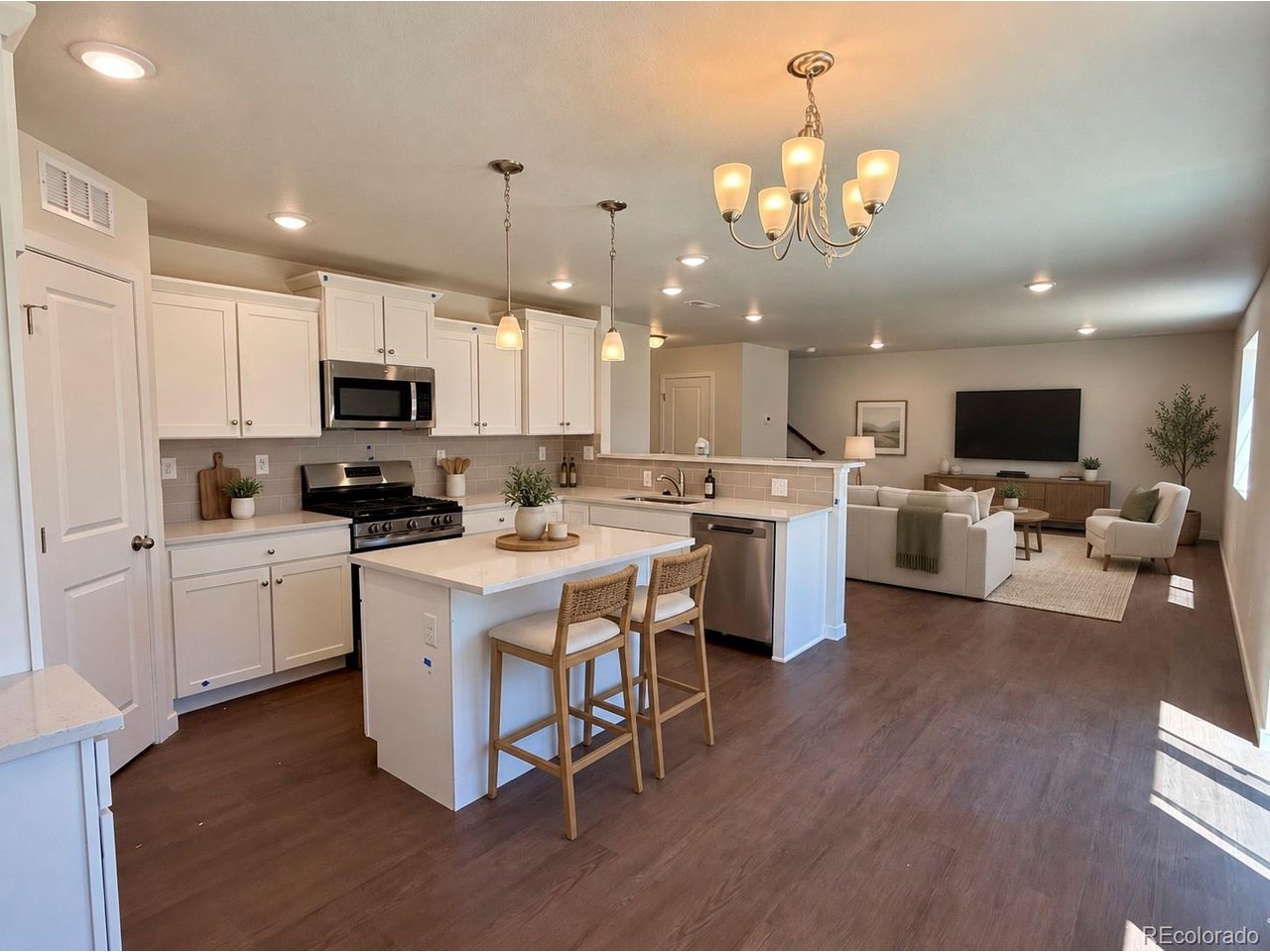 kitchen with white cabinetry, center island with two stools, stainless steel range and microwave, open sightline to a living room with sofa and wall-mounted TV