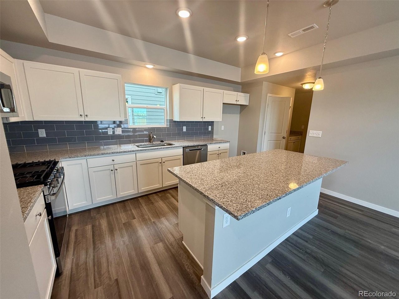 kitchen with center island, granite countertops, white cabinets, gray subway-tile backsplash, and pendant lights