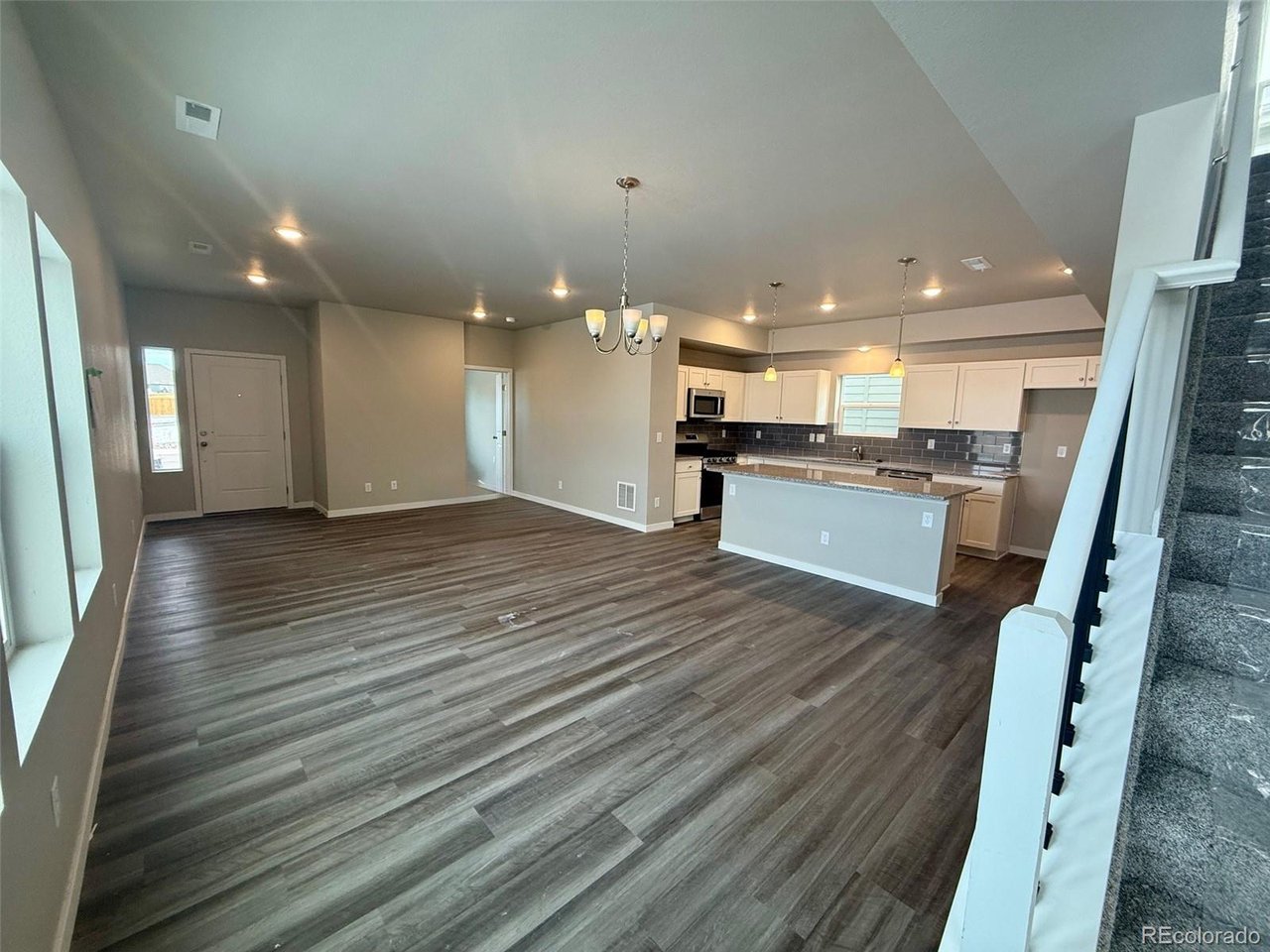 Great room and kitchen with vaulted ceiling, island, pendant lights, and gray wood-look flooring