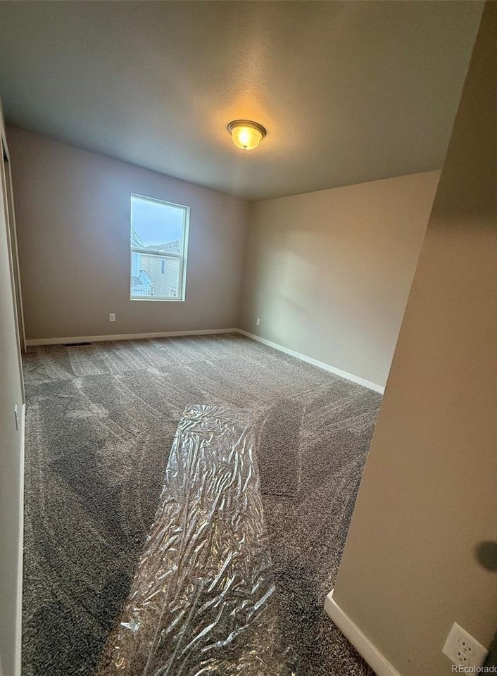 bedroom with single window, flush-mount ceiling light, neutral walls, and new carpeting with protective plastic runner