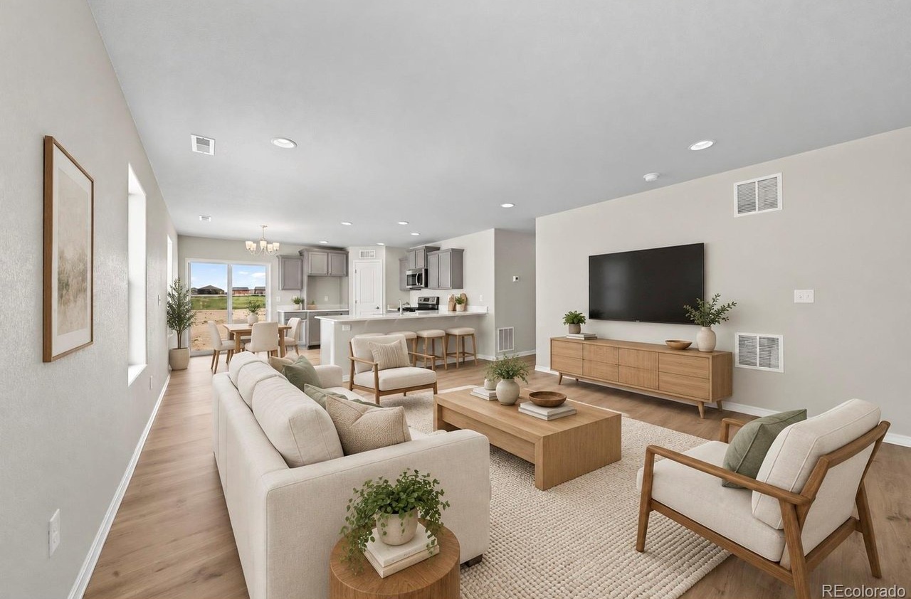 Great room with neutral walls, recessed lighting, wood-toned media console and open view into a kitchen with island and dining area beyond.